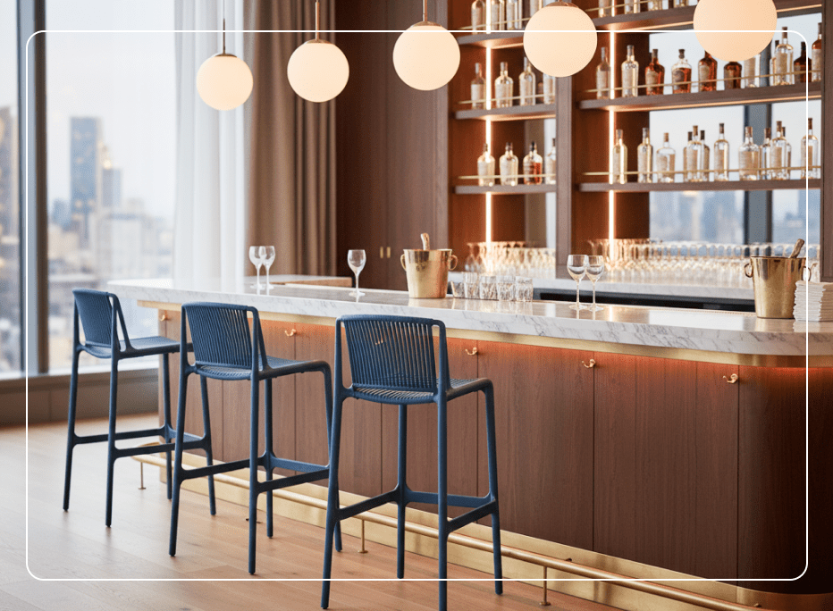 Three navy blue commercial bar stools with slatted backs arranged at a marble-topped hotel bar counter with warm wood paneling, brass accents, and globe pendant lighting.
